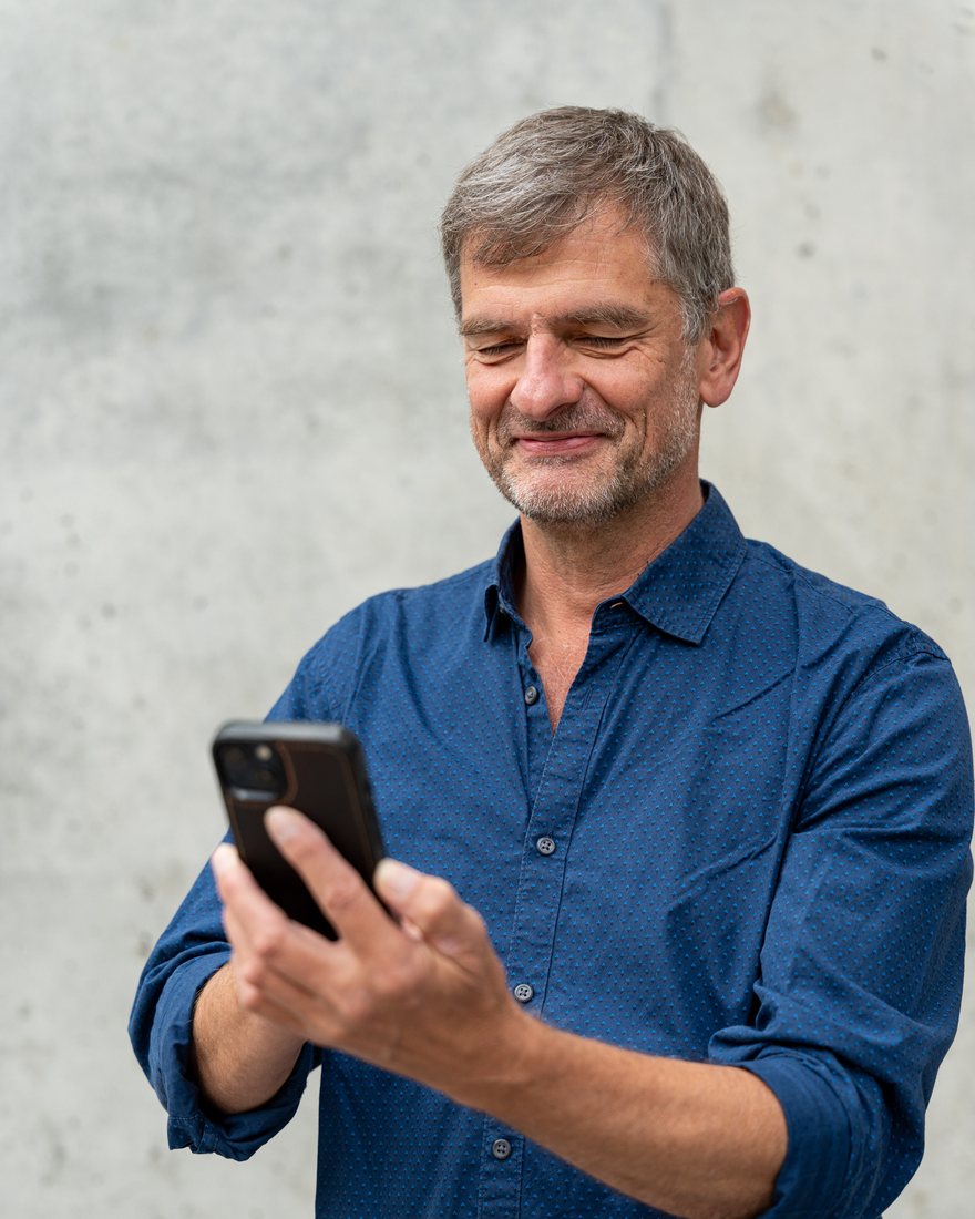 Jens Geithner schaut lächelnd auf sein Smartphone